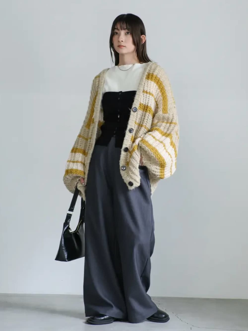 イエロー系のカーディガン/ボレロ、ホワイト系のニット/セーター、ブラック系のハンドバッグを着用したレディースの秋コーディネートの2枚目の写真