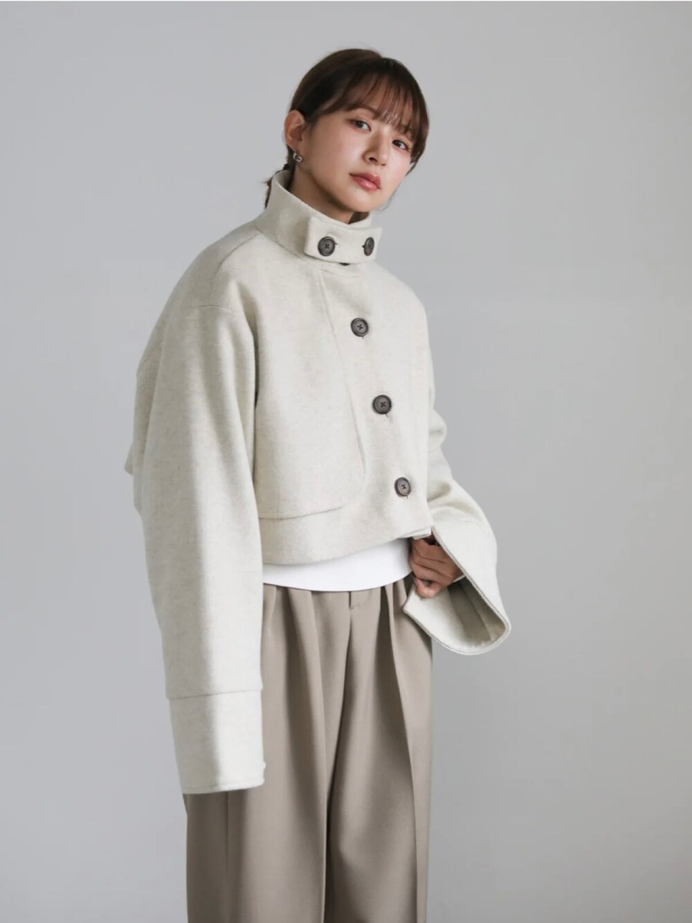 ベージュ系のステンカラーコート、ホワイト系のニット/セーター、グリーン系のベストを着用したレディースの冬コーディネートの3枚目の写真