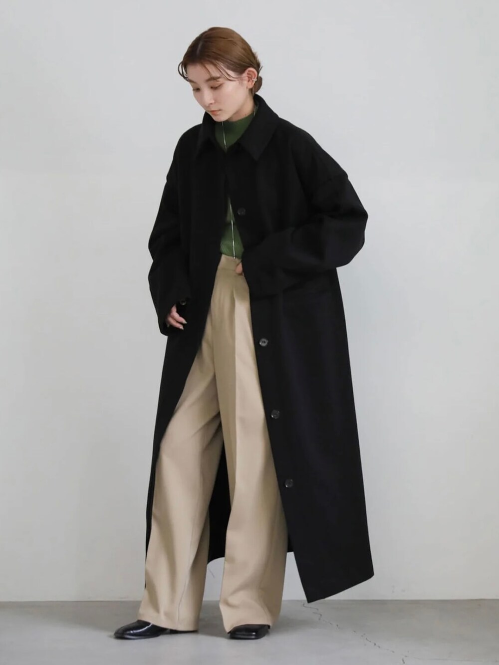 ベージュ系のスラックス、グリーン系のニット/セーター、ブラック系のステンカラーコートを着用したレディースの秋コーディネートの5枚目の写真