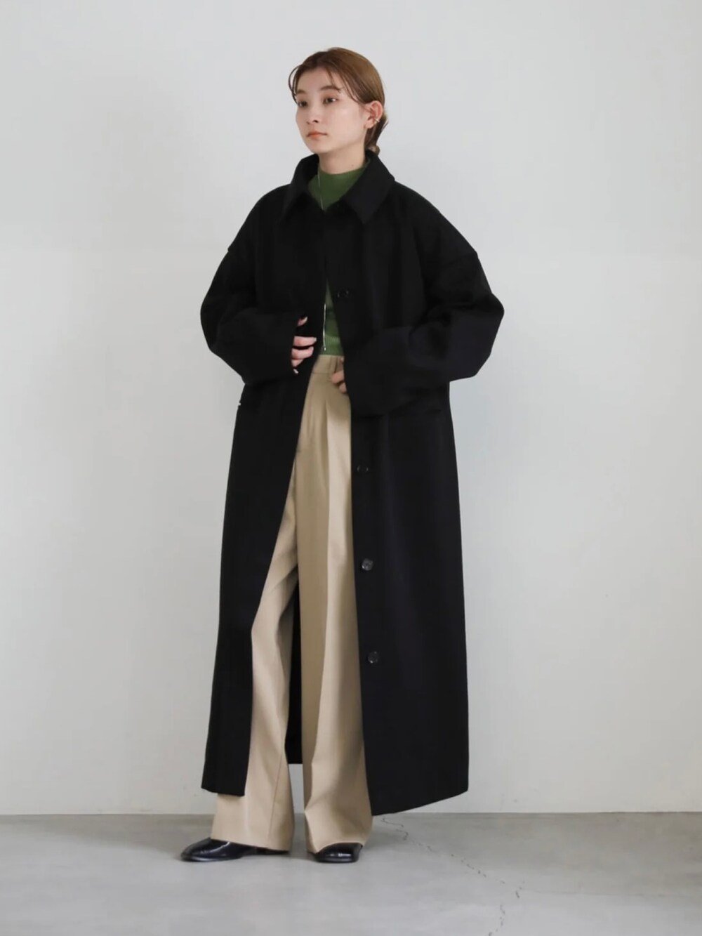 ベージュ系のスラックス、グリーン系のニット/セーター、ブラック系のステンカラーコートを着用したレディースの秋コーディネートの2枚目の写真