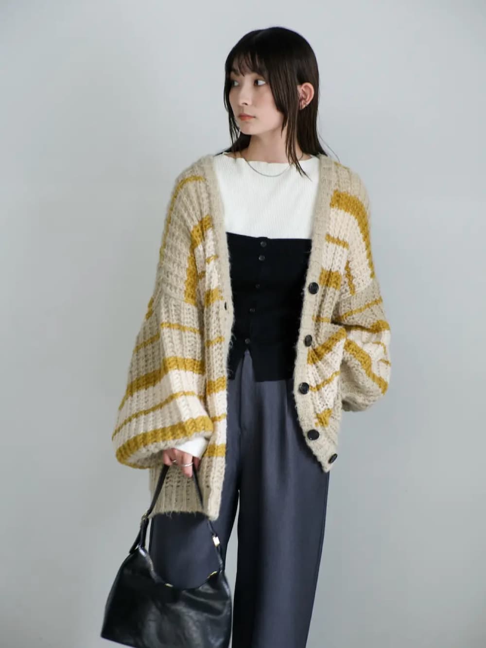 イエロー系のカーディガン/ボレロ、ホワイト系のニット/セーター、ブラック系のハンドバッグを着用したレディースの秋コーディネートの4枚目の写真