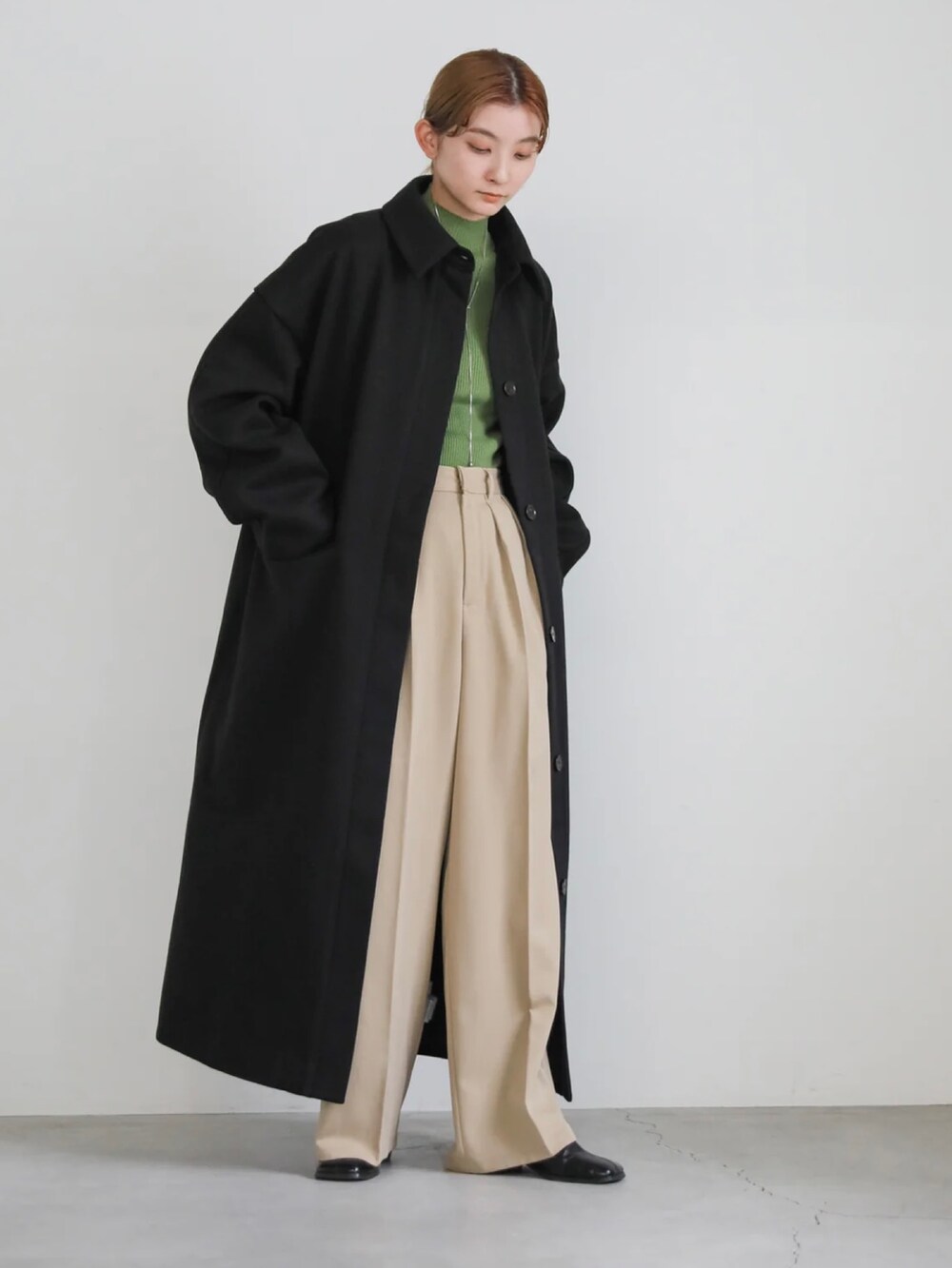 ベージュ系のスラックス、グリーン系のニット/セーター、ブラック系のステンカラーコートを着用したレディースの秋コーディネートの4枚目の写真