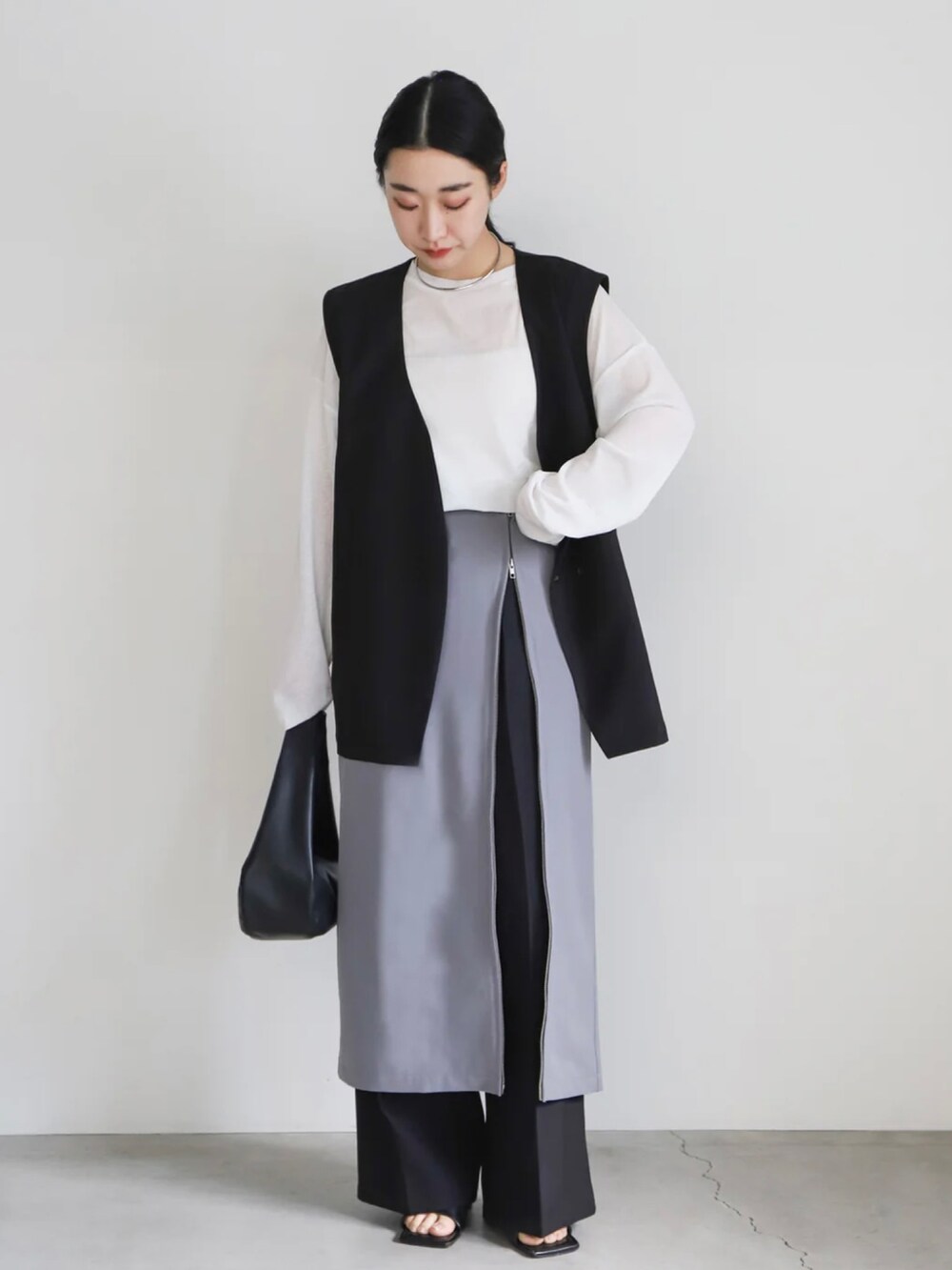 ブラック系のベスト、グレー系のスカート、ホワイト系のTシャツ/カットソーを着用したレディースの春コーディネートの2枚目の写真