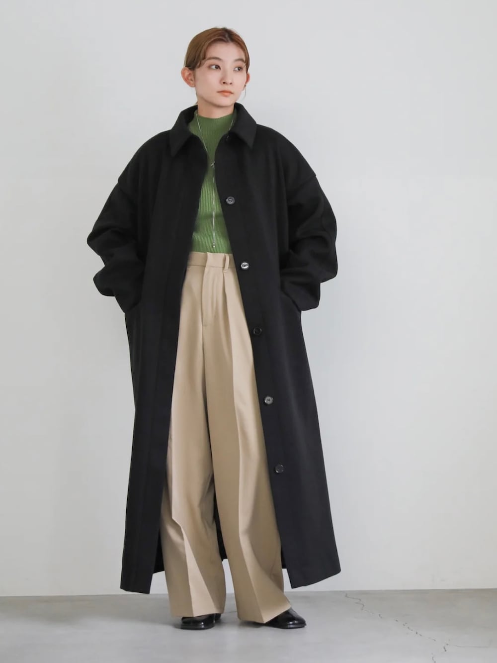 ベージュ系のスラックス、グリーン系のニット/セーター、ブラック系のステンカラーコートを着用したレディースの秋コーディネートの3枚目の写真