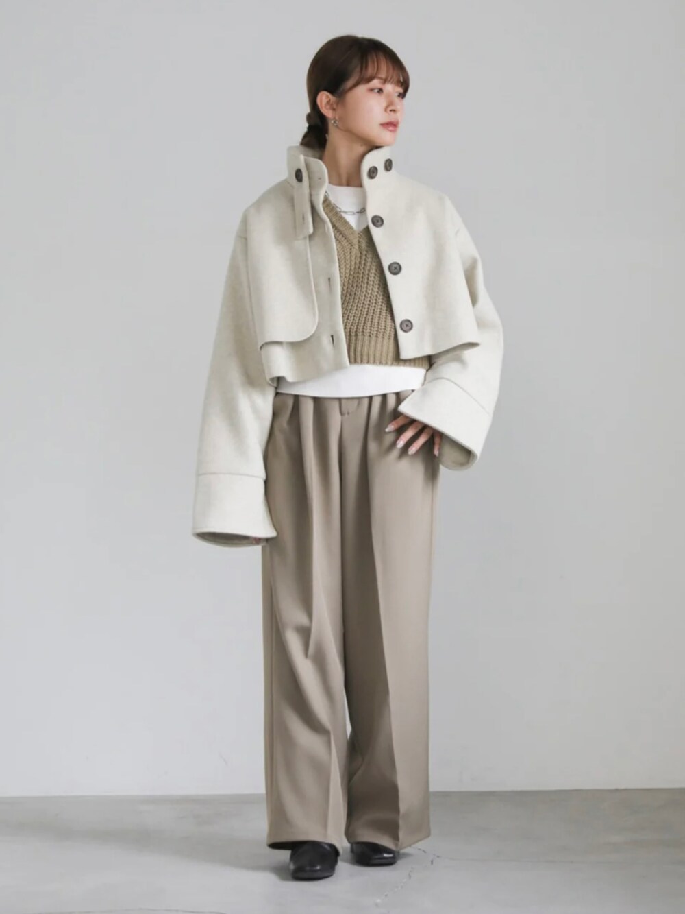 ベージュ系のステンカラーコート、ホワイト系のニット/セーター、グリーン系のベストを着用したレディースの冬コーディネートの4枚目の写真