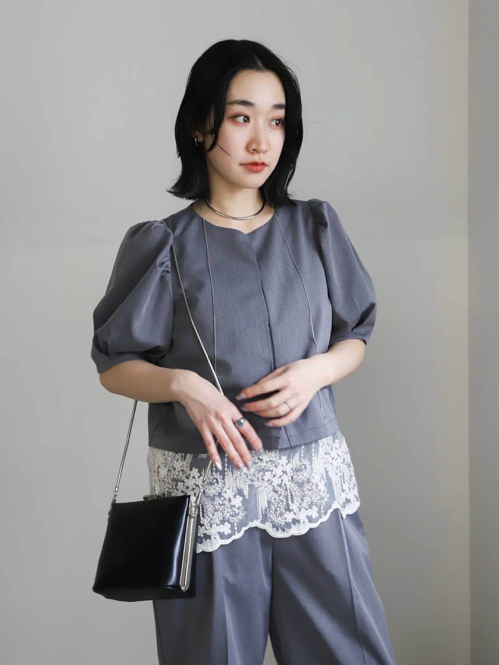 グレー系のセットアップ、ブラック系のパンプス、ブラック系のショルダーバッグを着用したレディースの春コーディネートの5枚目の写真