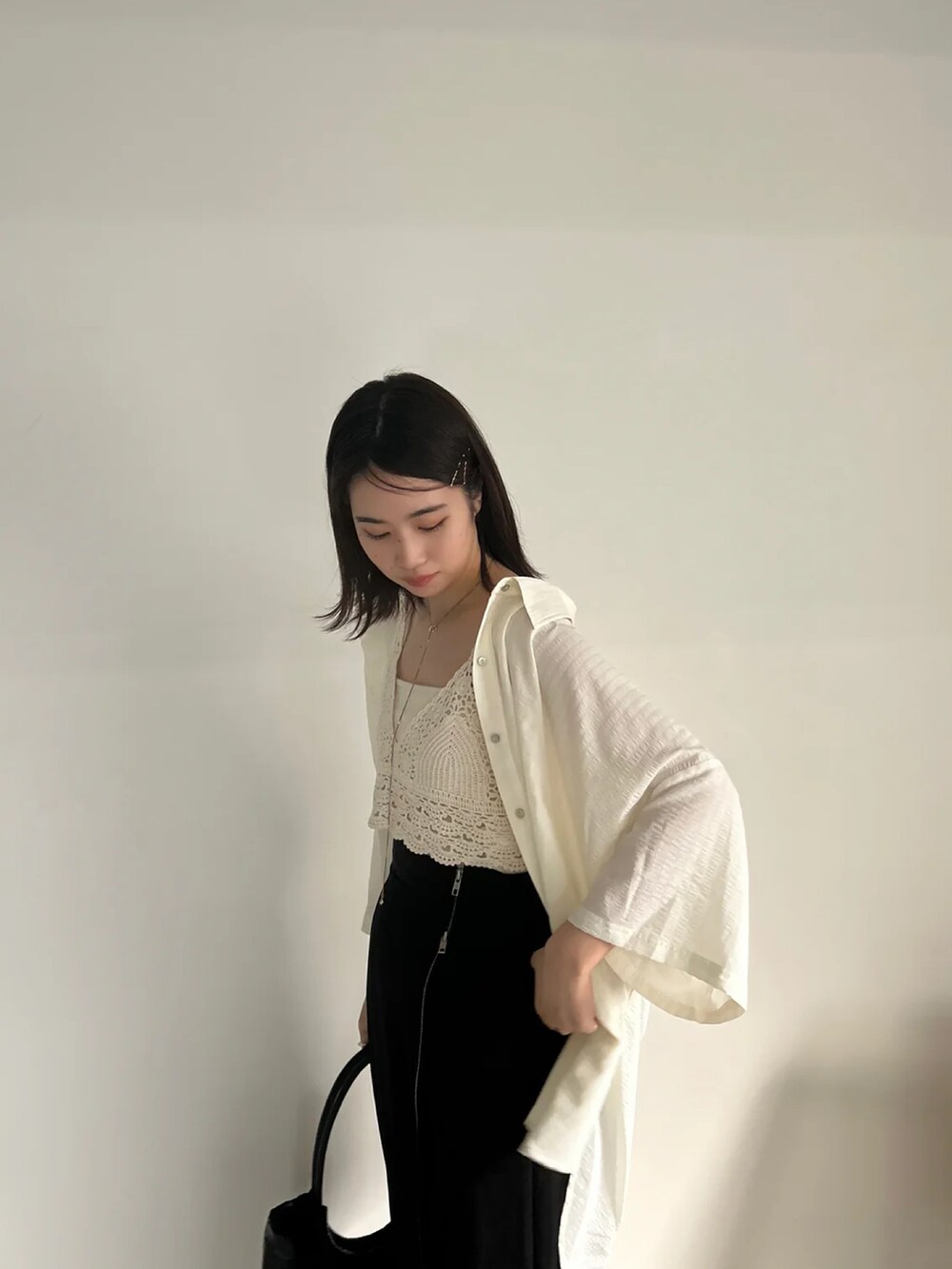 ブラック系のスカート、ホワイト系のベスト、グリーン系のキャミソールを着用したレディースの夏コーディネートの2枚目の写真