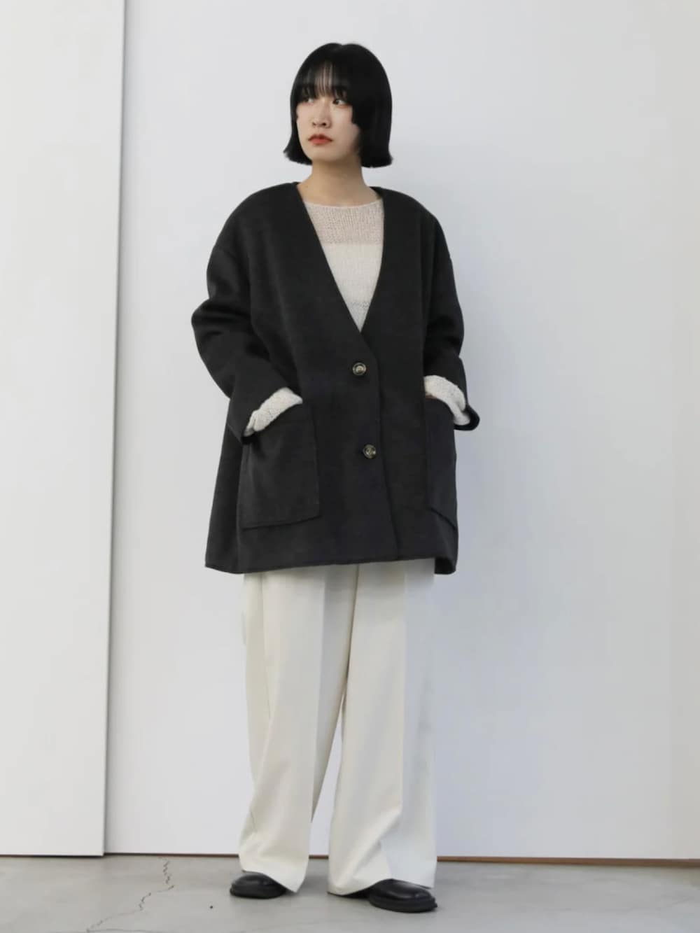 ブラック系のノーカラーコート、ホワイト系のニット/セーター、ホワイト系のスラックスを着用したレディースの秋コーディネートの3枚目の写真