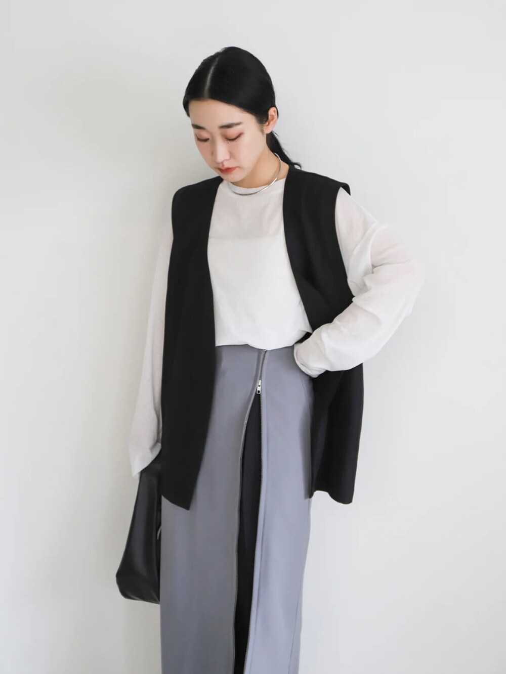 ブラック系のベスト、グレー系のスカート、ホワイト系のTシャツ/カットソーを着用したレディースの春コーディネートの4枚目の写真