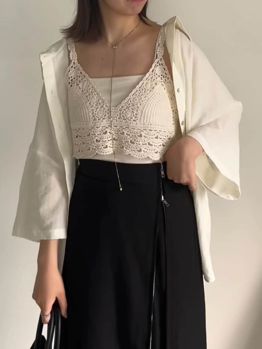 ブラック系のスカート、ホワイト系のベスト、グリーン系のキャミソールを着用したレディースの夏コーディネートの3枚目の写真