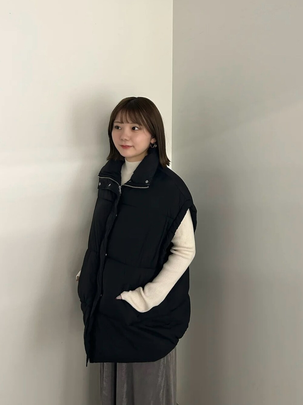 ブラック系のダウンベスト、ホワイト系のニット/セーター、グレー系のスカートを着用したレディースの秋コーディネートの4枚目の写真