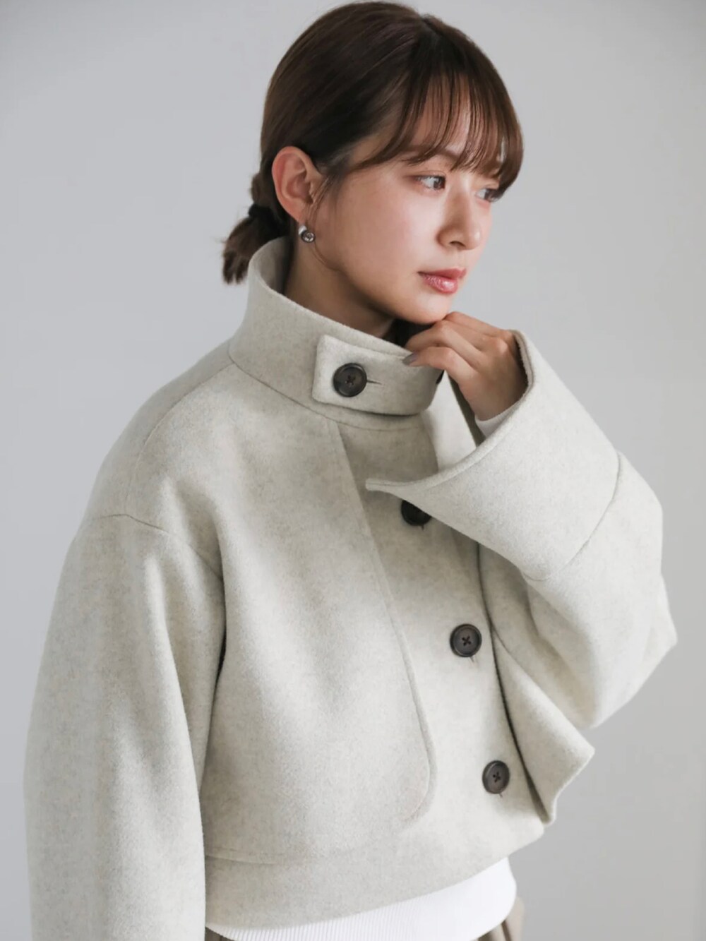 ベージュ系のステンカラーコート、ホワイト系のニット/セーター、グリーン系のベストを着用したレディースの冬コーディネートの2枚目の写真