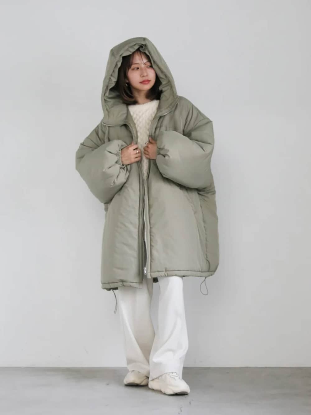 グリーン系のダウンジャケット/コート、ホワイト系のニット/セーター、ホワイト系のスラックスを着用したレディースの冬コーディネートの2枚目の写真