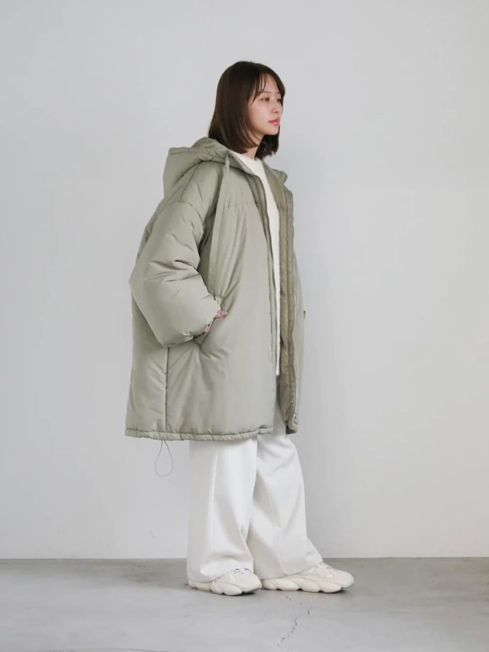 グリーン系のダウンジャケット/コート、ホワイト系のニット/セーター、ホワイト系のスラックスを着用したレディースの冬コーディネートの3枚目の写真