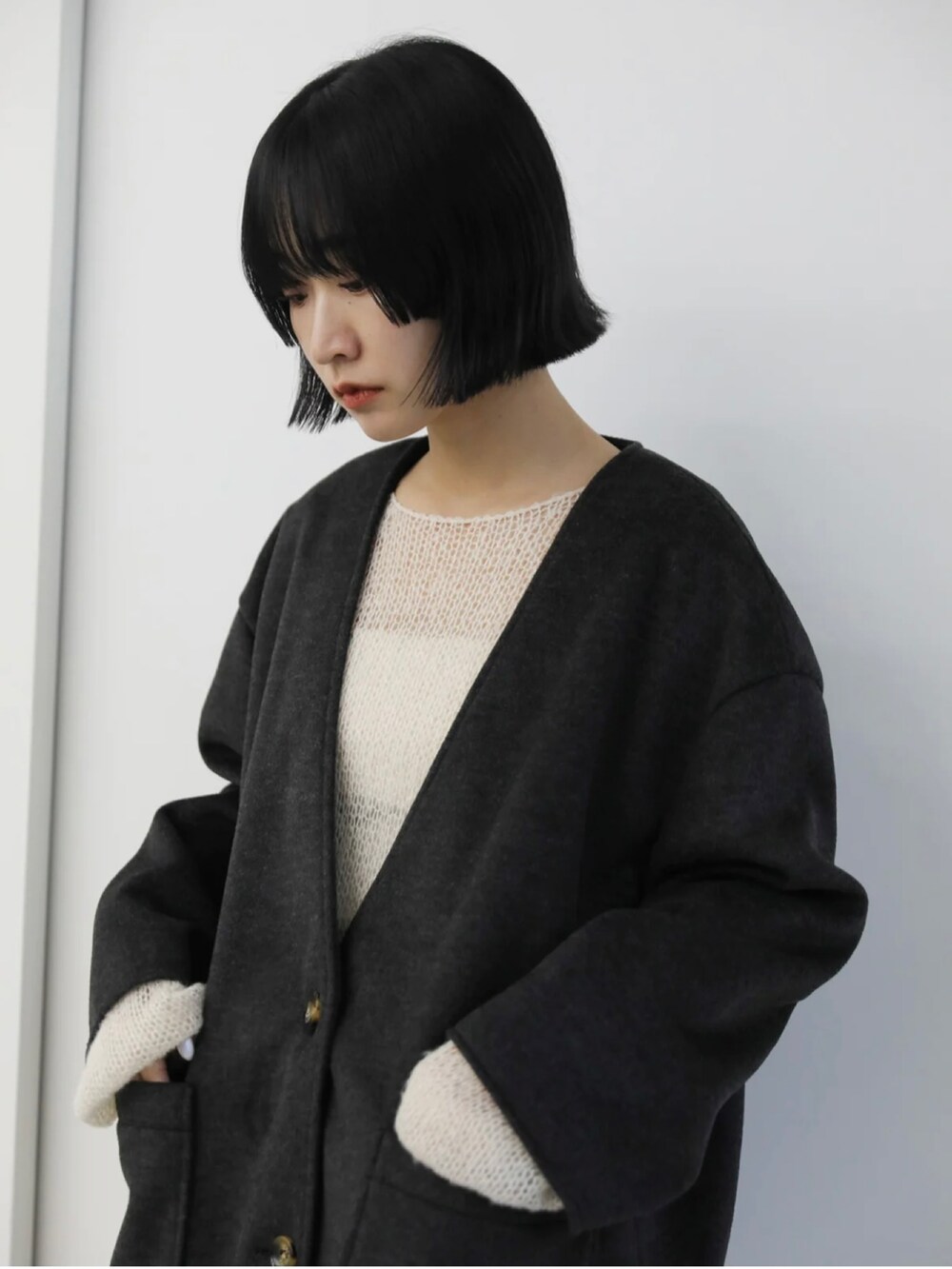 ブラック系のノーカラーコート、ホワイト系のニット/セーター、ホワイト系のスラックスを着用したレディースの秋コーディネートの2枚目の写真