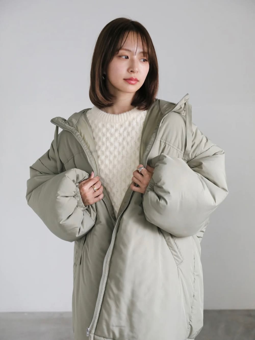 グリーン系のダウンジャケット/コート、ホワイト系のニット/セーター、ホワイト系のスラックスを着用したレディースの冬コーディネートの5枚目の写真