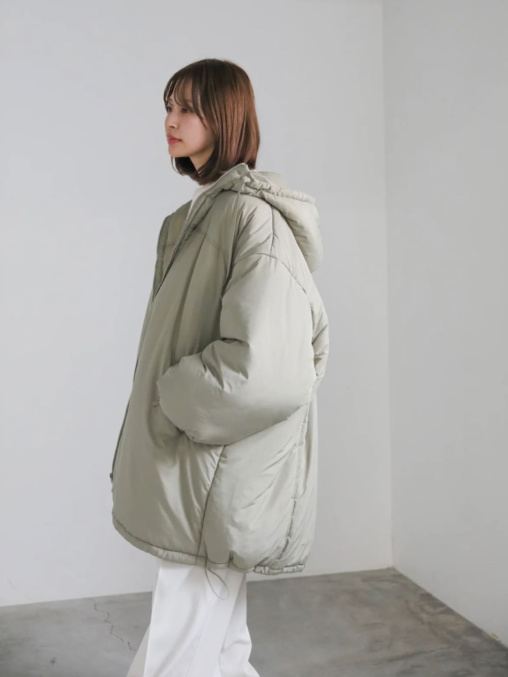 グリーン系のダウンジャケット/コート、ホワイト系のニット/セーター、ホワイト系のスラックスを着用したレディースの冬コーディネートの4枚目の写真