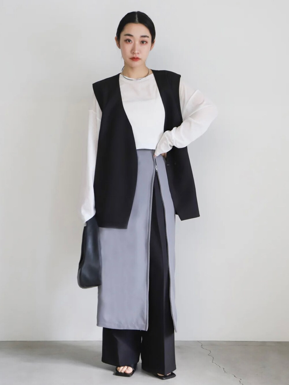 ブラック系のベスト、グレー系のスカート、ホワイト系のTシャツ/カットソーを着用したレディースの春コーディネートの3枚目の写真