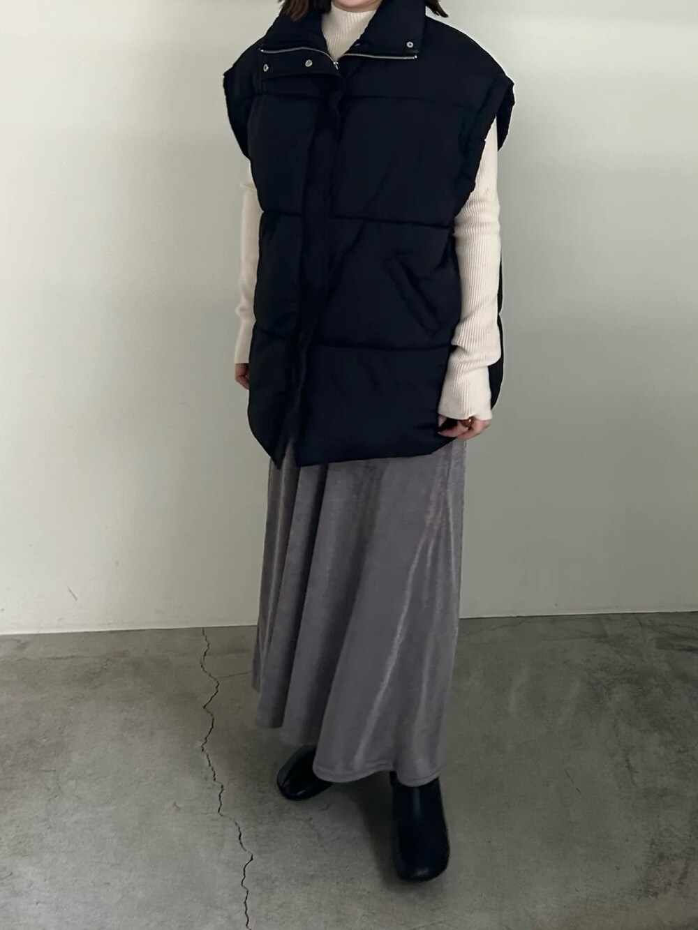 ブラック系のダウンベスト、ホワイト系のニット/セーター、グレー系のスカートを着用したレディースの秋コーディネートの3枚目の写真