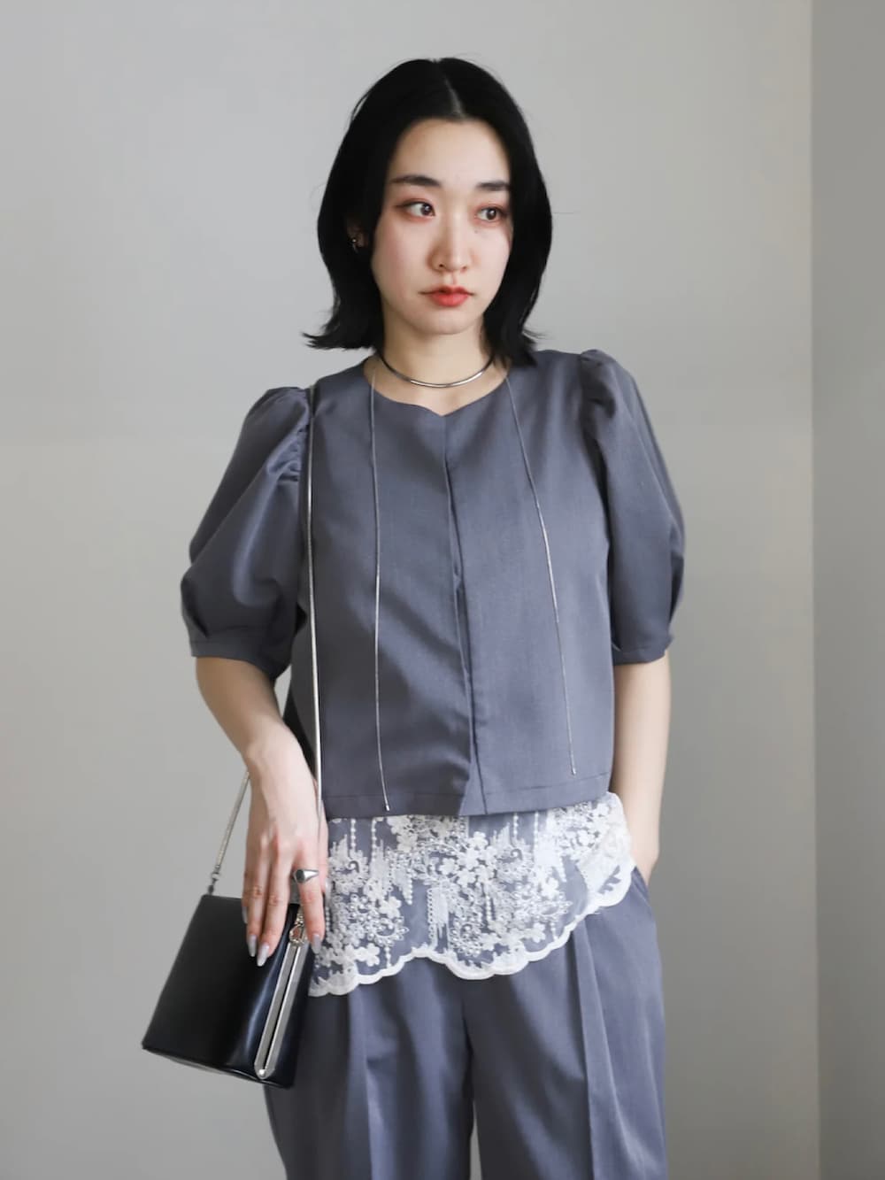 グレー系のセットアップ、ブラック系のパンプス、ブラック系のショルダーバッグを着用したレディースの春コーディネートの4枚目の写真
