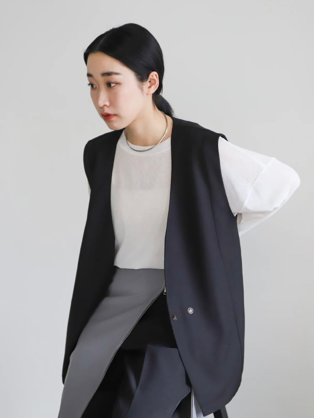ブラック系のベスト、グレー系のスカート、ホワイト系のTシャツ/カットソーを着用したレディースの春コーディネートの5枚目の写真