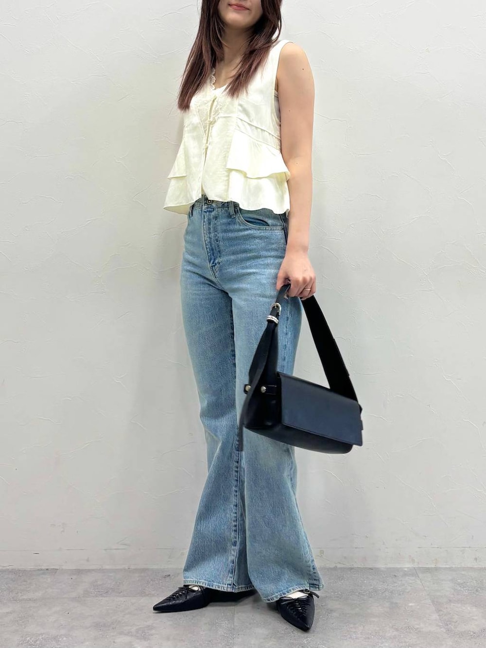 ブルー系のデニムパンツ、ブラック系のショルダーバッグ、ホワイト系のベストを着用したレディースの春コーディネートの2枚目の写真