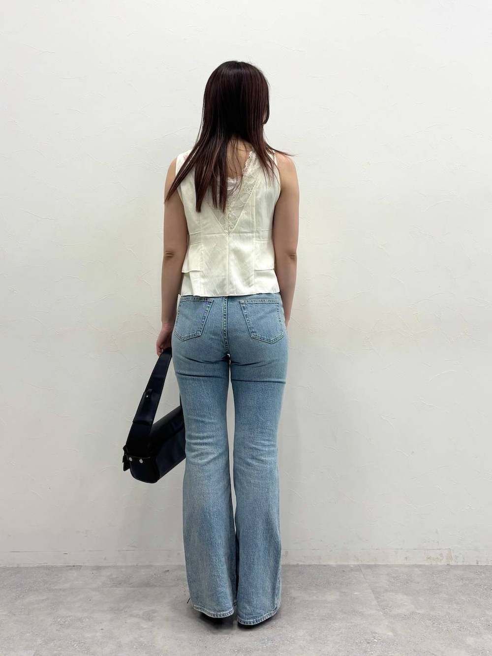 ブルー系のデニムパンツ、ブラック系のショルダーバッグ、ホワイト系のベストを着用したレディースの春コーディネートの4枚目の写真