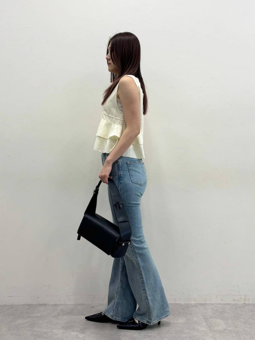 ブルー系のデニムパンツ、ブラック系のショルダーバッグ、ホワイト系のベストを着用したレディースの春コーディネートの3枚目の写真