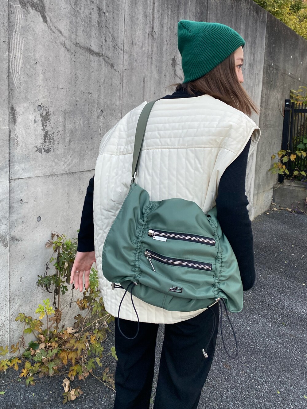 ホワイト系のノーカラーコート、ブラック系のブーツ、グリーン系のショルダーバッグを着用したレディースの秋コーディネートの4枚目の写真