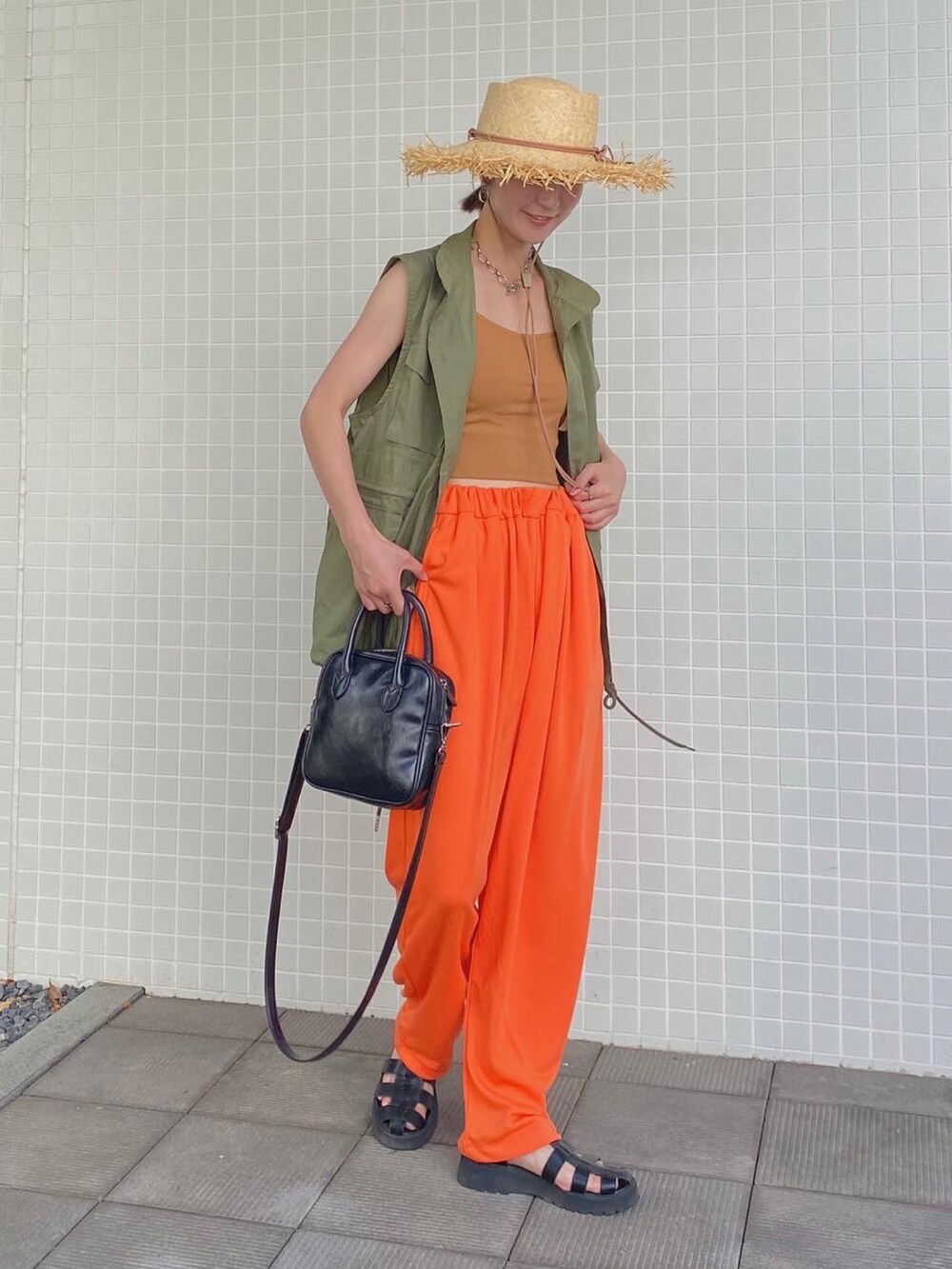 オレンジ系のスウェットパンツ、ブラック系のサンダル、グリーン系のベストを着用したレディースの夏コーディネートの2枚目の写真