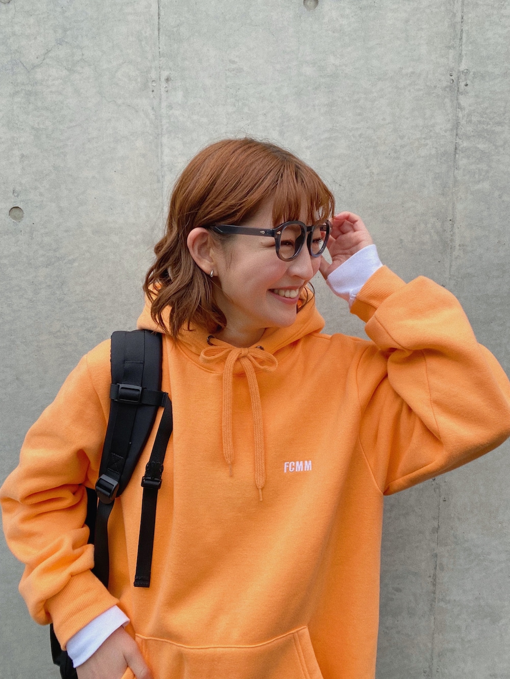 オレンジ系のパーカー、ブラック系のバックパック/リュック、イエロー系のスラックスを着用したレディースの春コーディネートの3枚目の写真