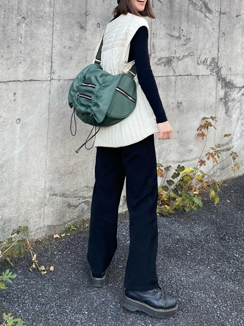 ホワイト系のノーカラーコート、ブラック系のブーツ、グリーン系のショルダーバッグを着用したレディースの秋コーディネートの2枚目の写真