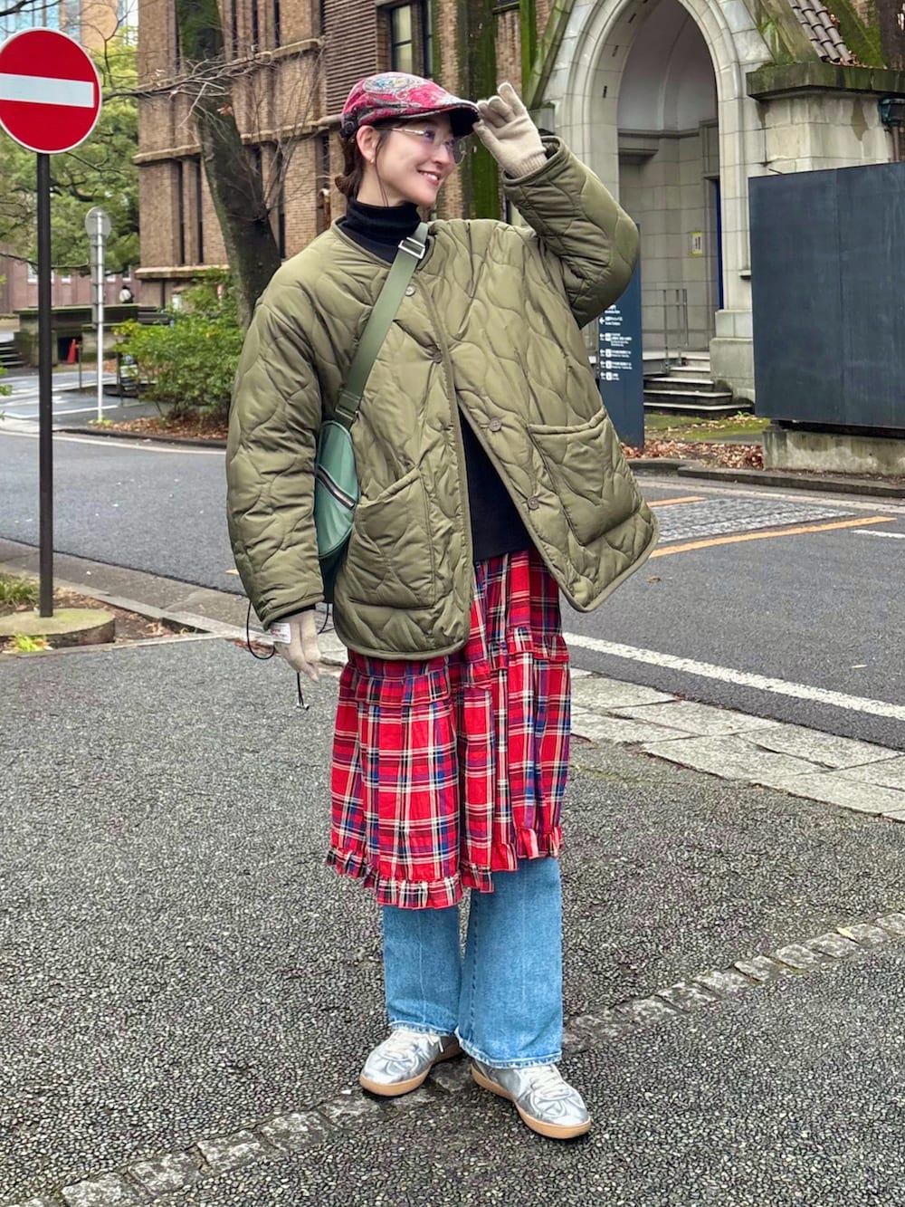 レッド系のワンピース、ブルー系のデニムパンツ、グリーン系のショルダーバッグを着用したレディースの春コーディネートの2枚目の写真