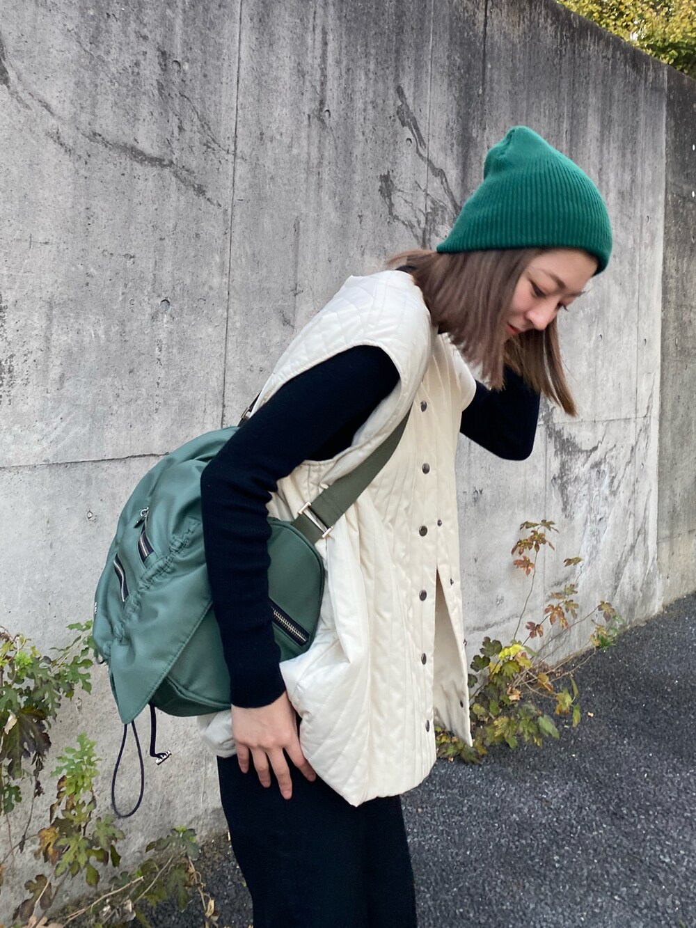 ホワイト系のノーカラーコート、ブラック系のブーツ、グリーン系のショルダーバッグを着用したレディースの秋コーディネートの5枚目の写真