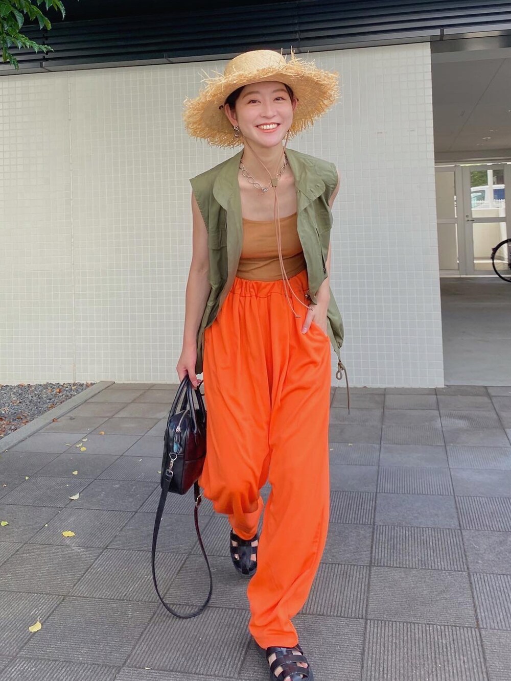 オレンジ系のスウェットパンツ、ブラック系のサンダル、グリーン系のベストを着用したレディースの夏コーディネートの3枚目の写真