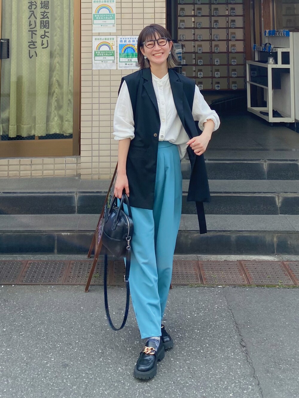 ブラック系のショルダーバッグ、ブルー系のスラックス、ブラック系のローファーを着用したレディースの春コーディネートの2枚目の写真