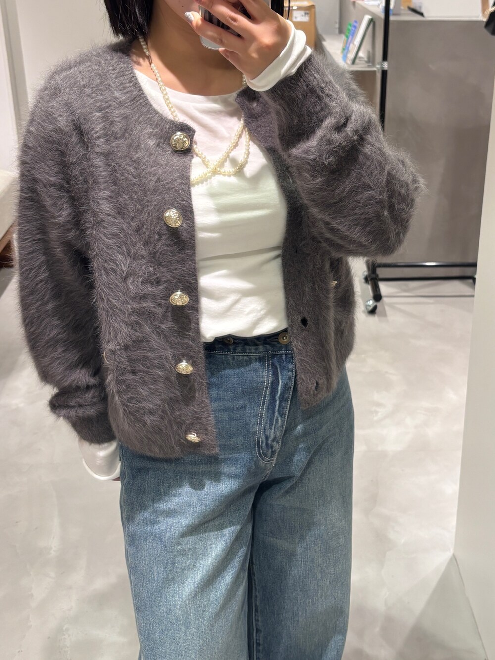 グレー系のニット/セーター、ブルー系のデニムパンツ、ホワイト系のTシャツ/カットソーを着用したレディースの秋コーディネートの2枚目の写真