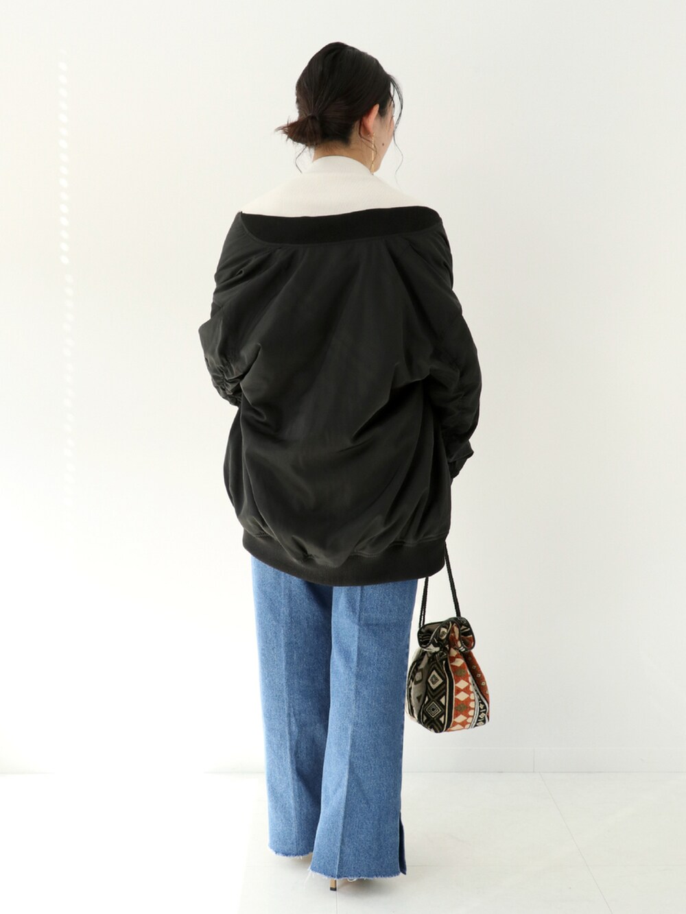 ブルー系のデニムパンツ、オレンジ系のショルダーバッグ、ブラック系のブルゾンを着用したレディースの秋コーディネートの2枚目の写真