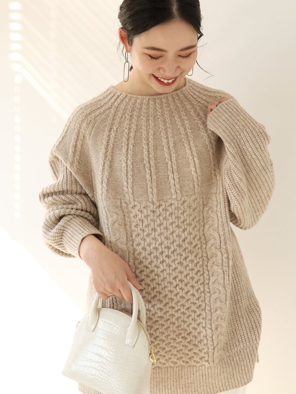 ベージュ系のニット/セーター、ホワイト系のスラックス、ホワイト系のショルダーバッグを着用したレディースの冬コーディネートの2枚目の写真