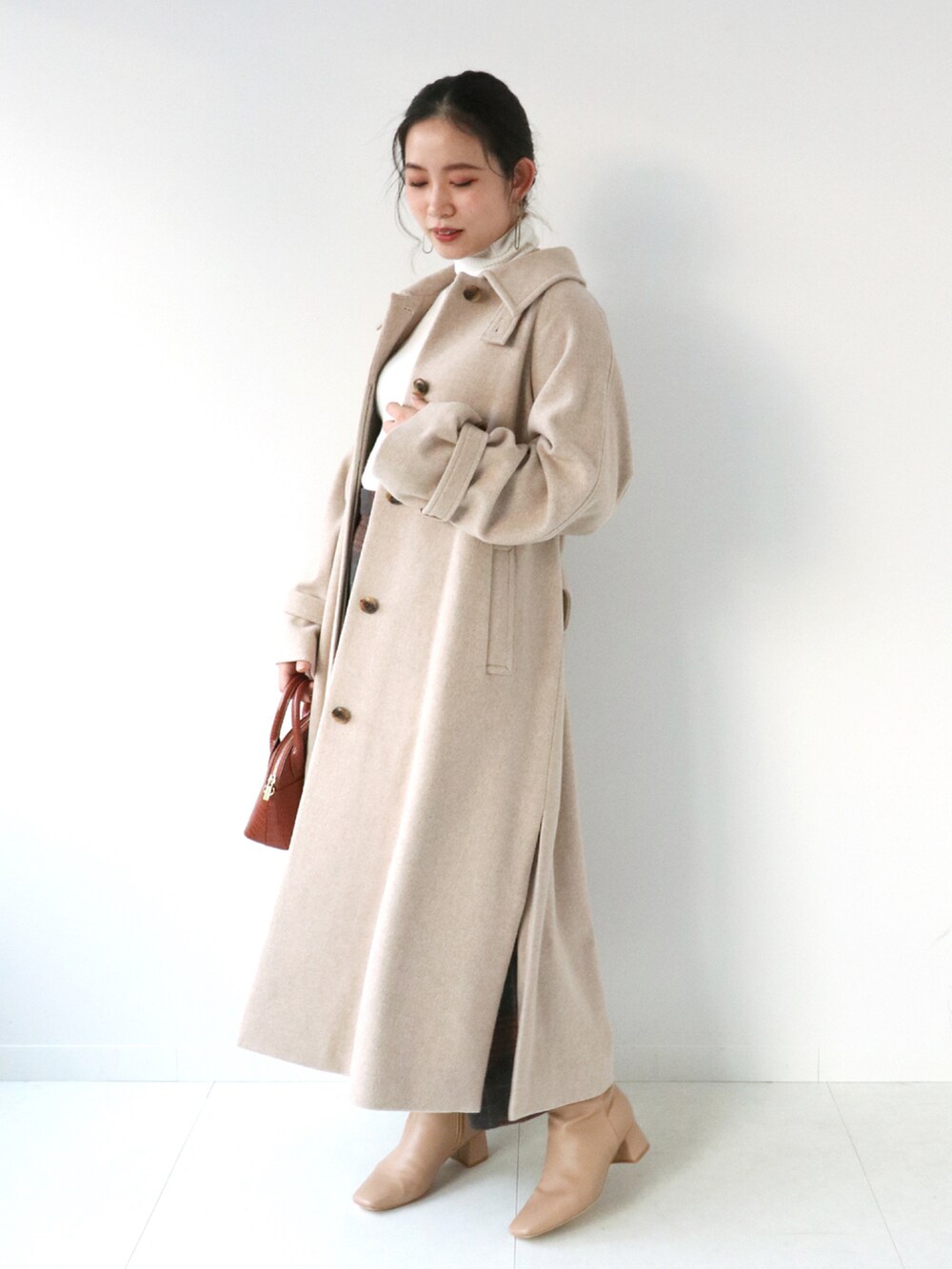 ブラウン系のスカート、ベージュ系のステンカラーコート、ホワイト系のニット/セーターを着用したレディースの冬コーディネートの2枚目の写真