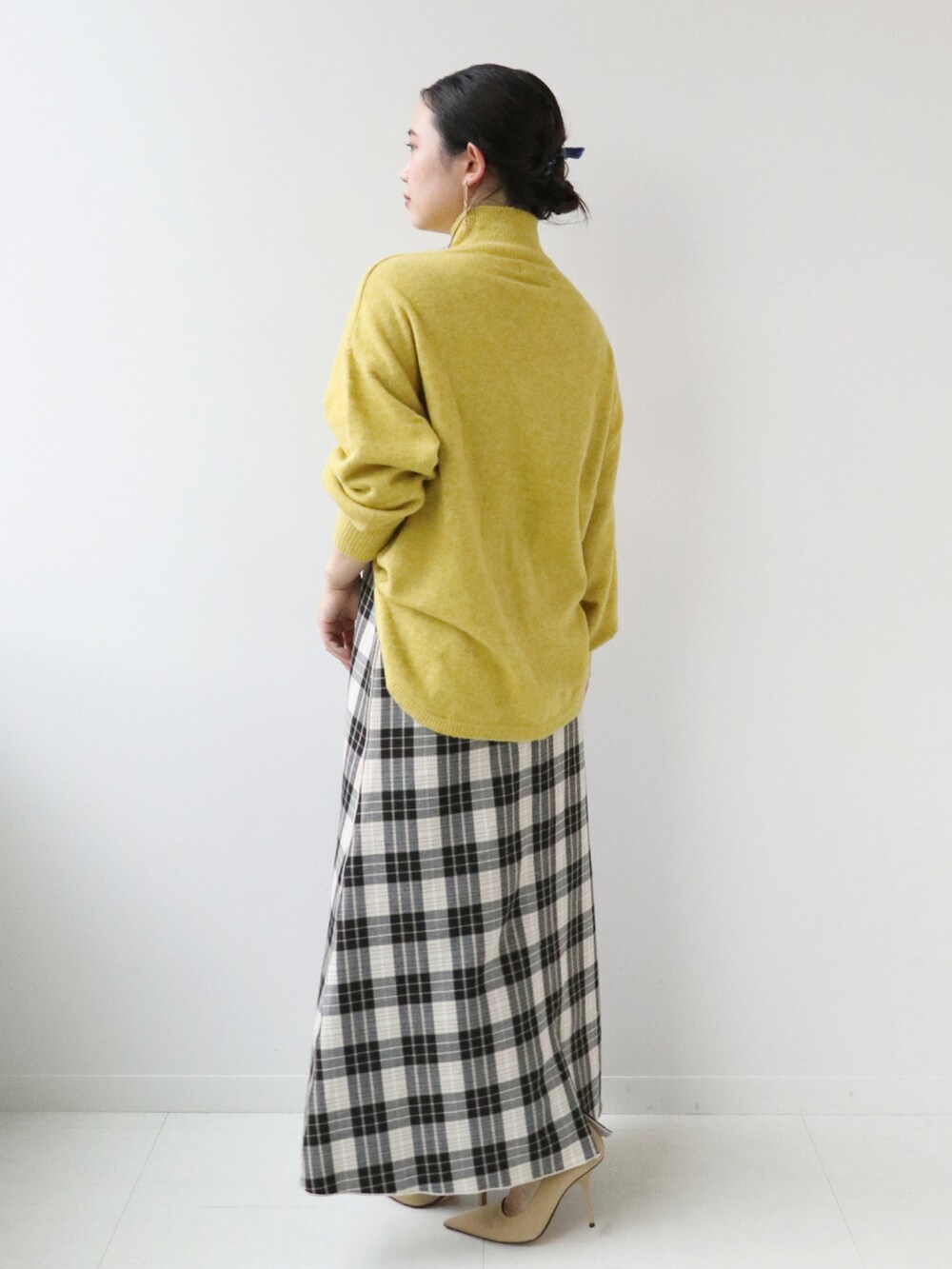 イエロー系のニット/セーター、ベージュ系のスカートを着用したレディースの秋コーディネートの2枚目の写真