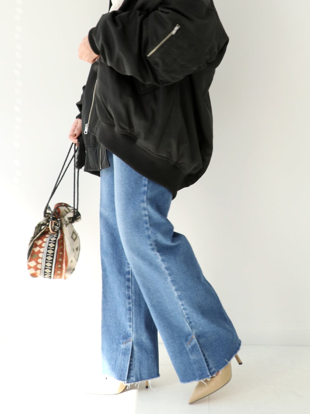 ブルー系のデニムパンツ、オレンジ系のショルダーバッグ、ブラック系のブルゾンを着用したレディースの秋コーディネートの3枚目の写真