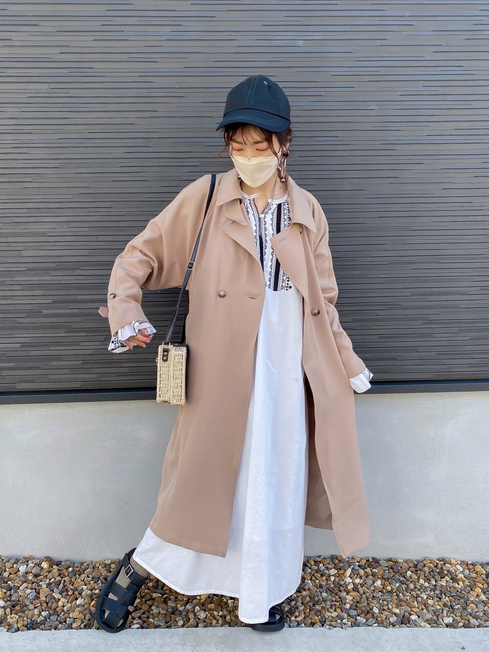 ベージュ系のトレンチコート、ホワイト系のワンピース、ブラック系のサンダルを着用したレディースの春コーディネートの2枚目の写真
