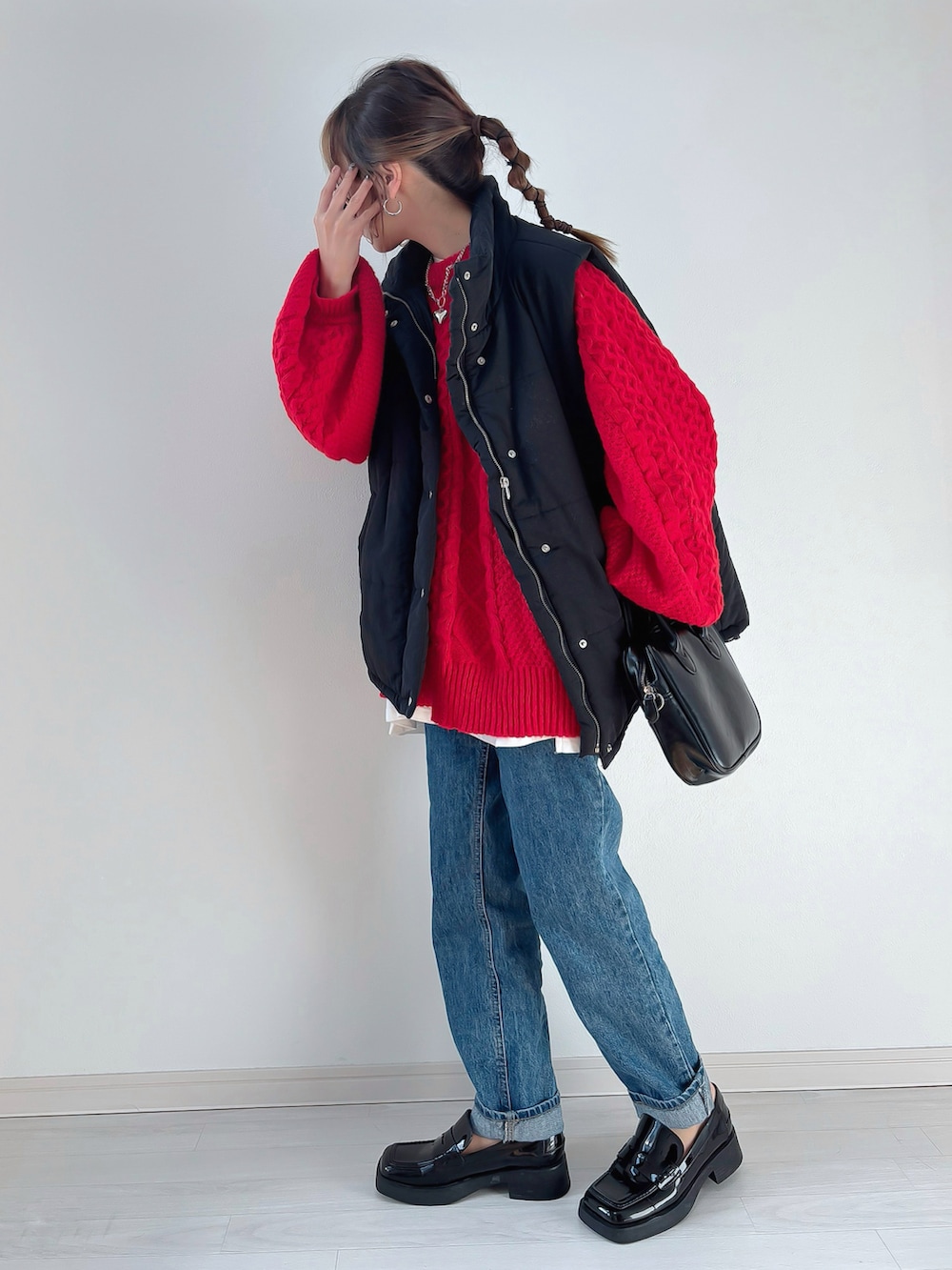 ブラック系のベスト、レッド系のニット/セーター、ブルー系のデニムパンツを着用したレディースの冬コーディネートの2枚目の写真