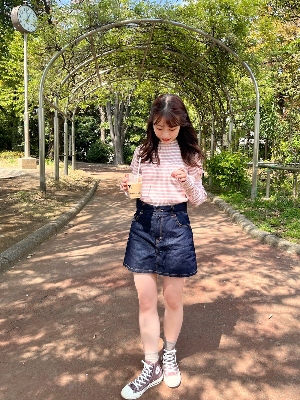 ブルー系のデニムスカート、ピンク系のニット/セーター、ブラウン系のスニーカーを着用したレディースの春コーディネートの2枚目の写真