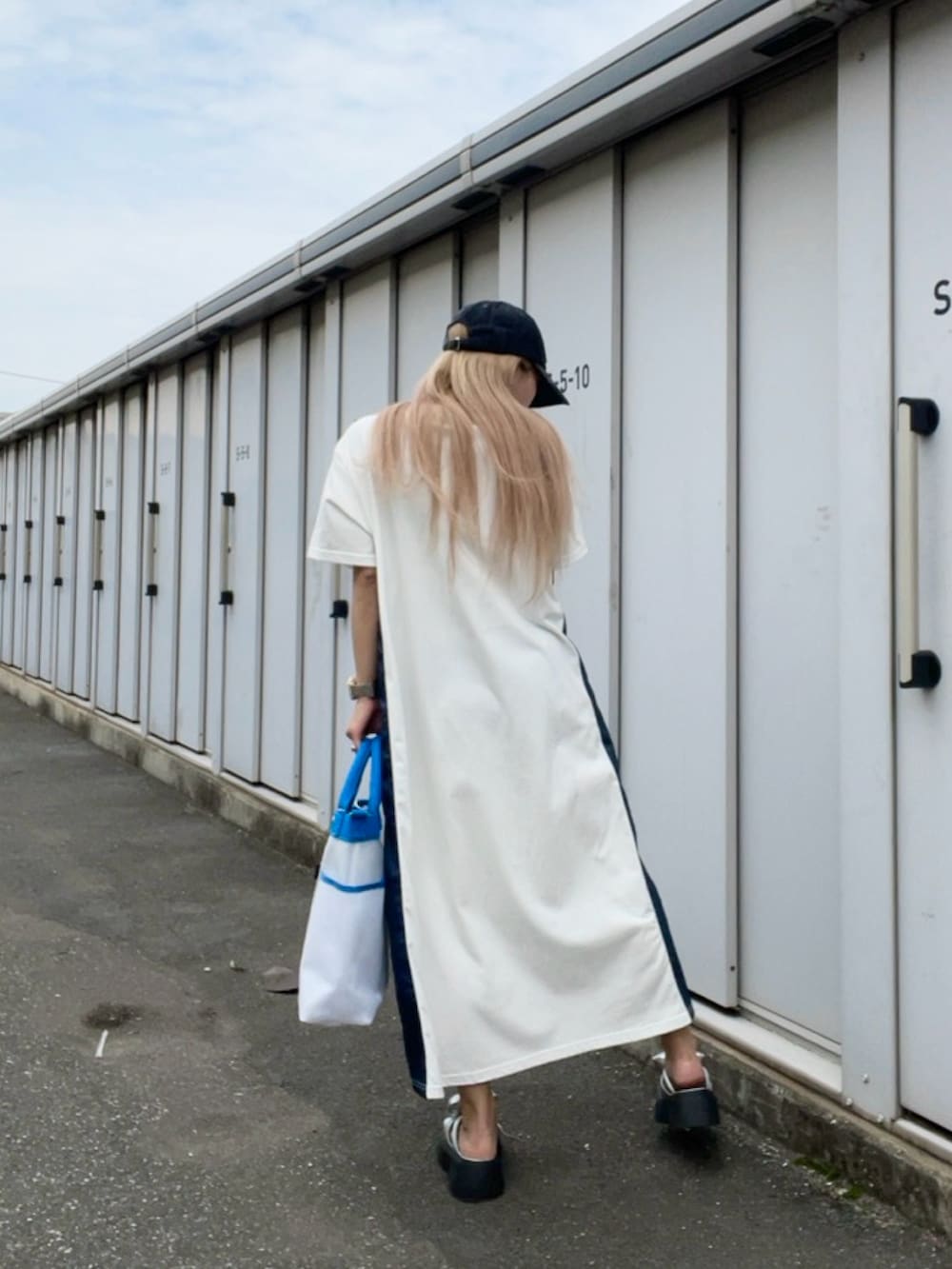 ブルー系のトートバッグ、ホワイト系のワンピース、ブラック系のキャップを着用したレディースの夏コーディネートの2枚目の写真