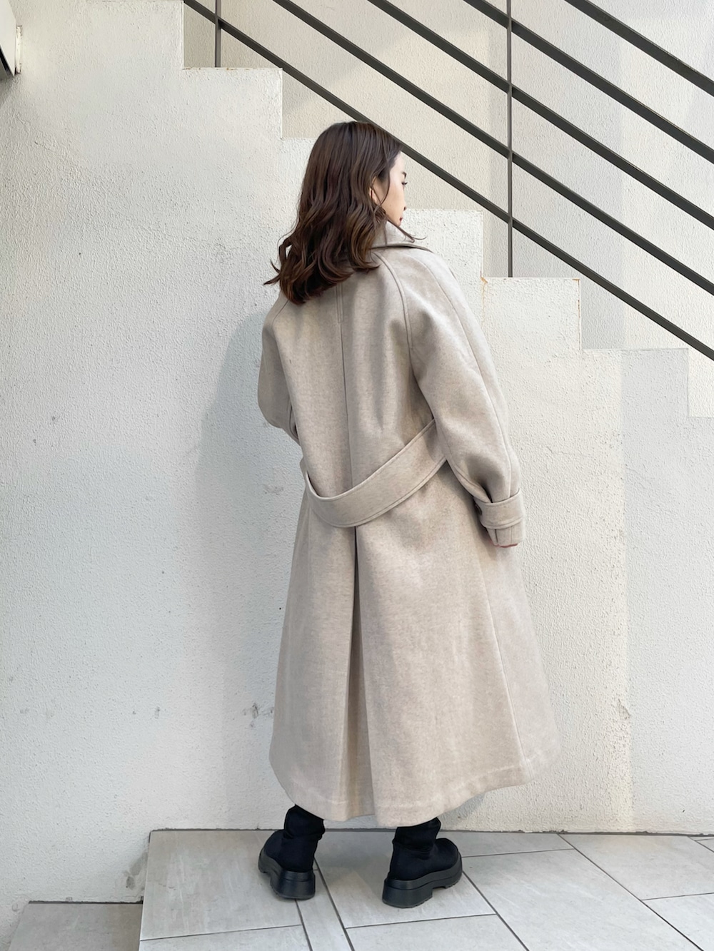 ベージュ系のステンカラーコート、ブラック系のブーツ、ブラック系のスカートを着用したレディースの秋コーディネートの2枚目の写真