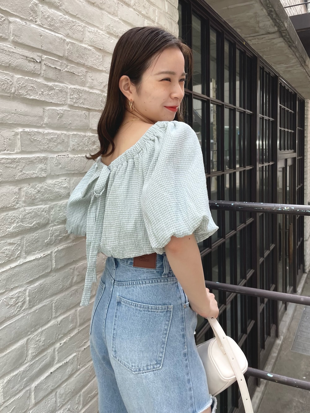 ブルー系のデニムパンツ、グリーン系のシャツ/ブラウス、ホワイト系のハンドバッグを着用したレディースの春コーディネートの2枚目の写真