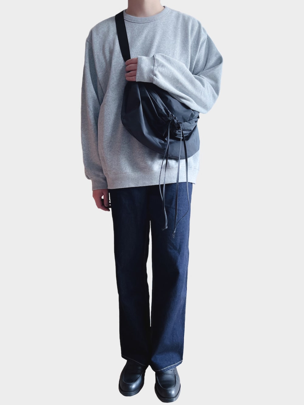 グレー系のスウェット、ブラック系のショルダーバッグ、ブルー系のデニムパンツを着用したメンズの冬コーディネートの2枚目の写真