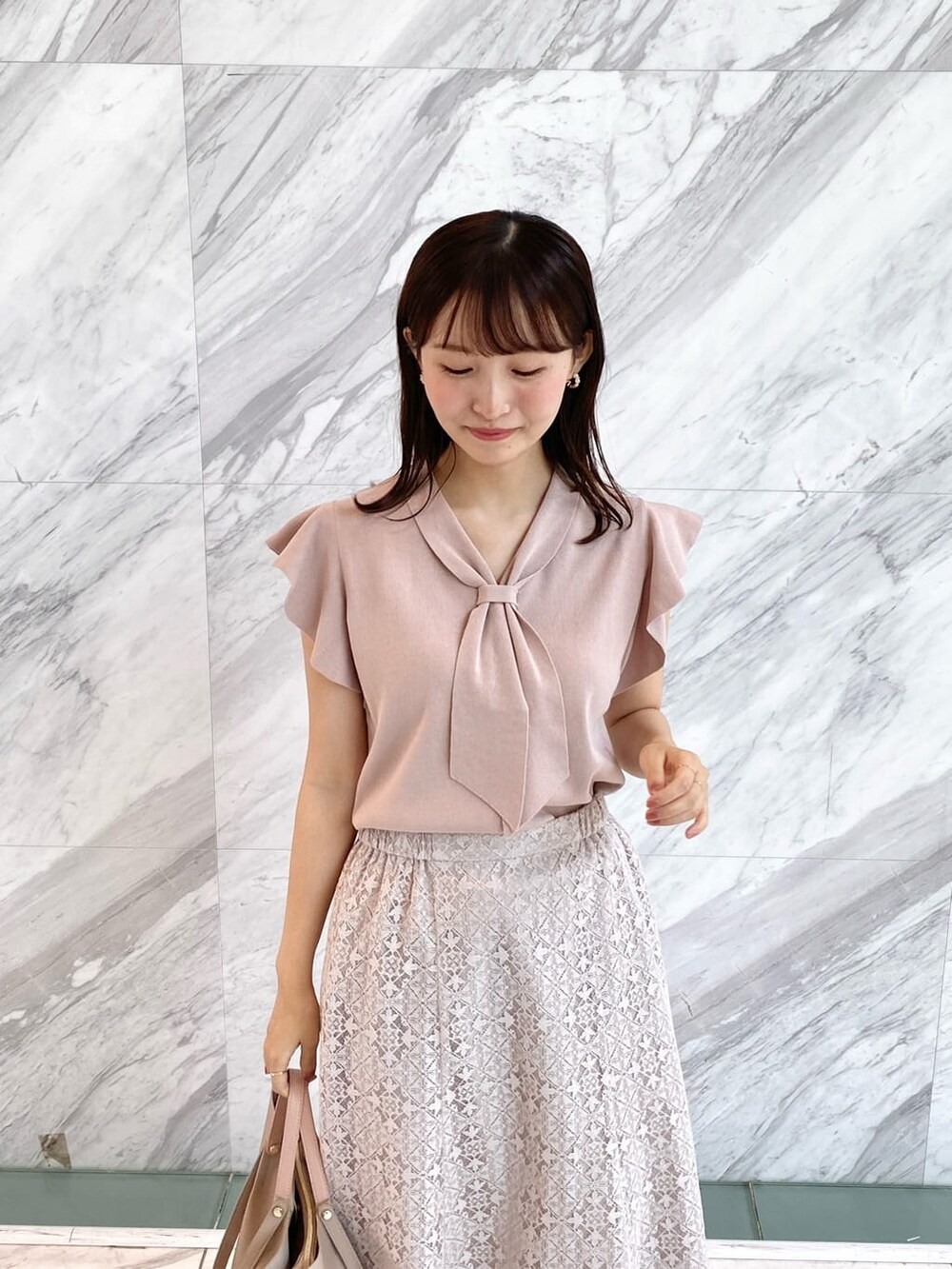 ピンク系のニット/セーター、ベージュ系のスカート、ベージュ系のトートバッグを着用したレディースの夏コーディネートの6枚目の写真